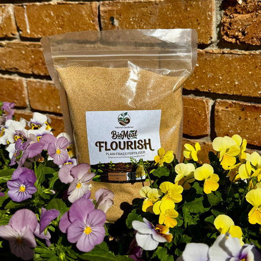 Bag of BioMed Flourish fertilizer with flowers in front of a brick wall